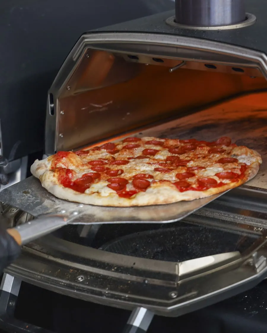 A finished pizza coming out of the portable high-temperature oven on a peel