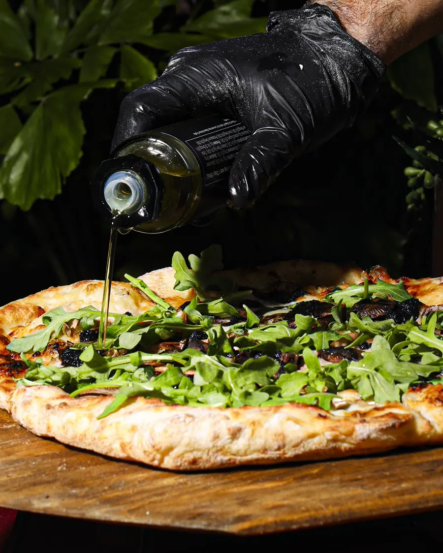 Olive oil finishing a wood-board arugula pizza at an event