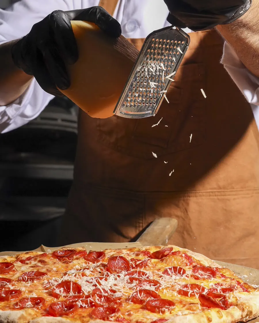A finished NY-style pepperoni pizza dusted with grated cheese